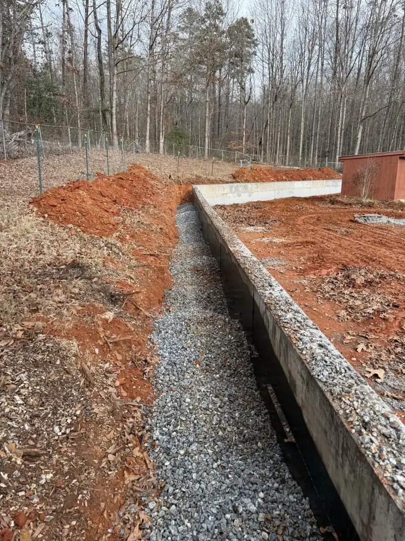 A gravel-lined footing trench running beside a formed concrete wall
