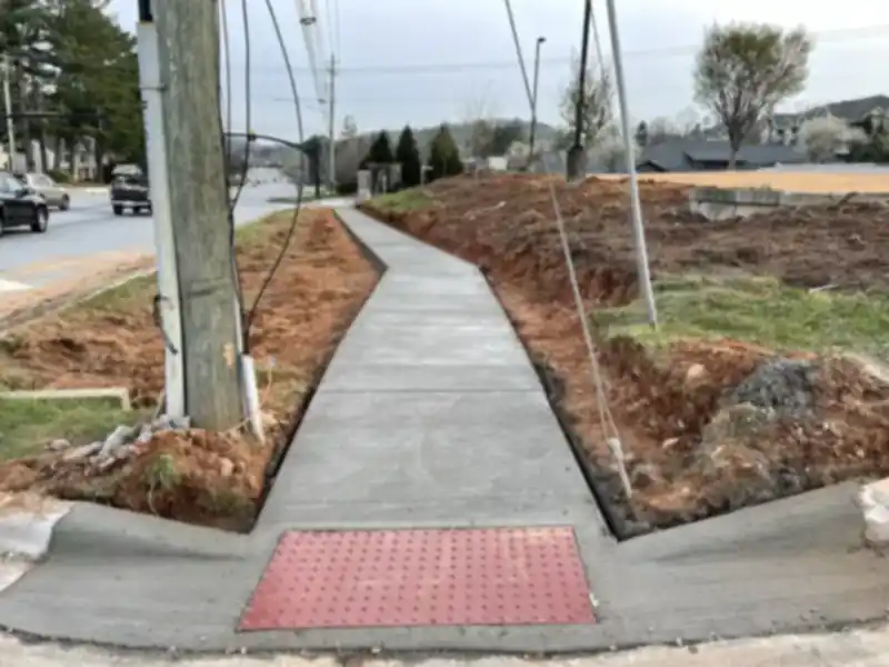 A concrete sidewalk with a red curb-ramp warning pad beside a busy road