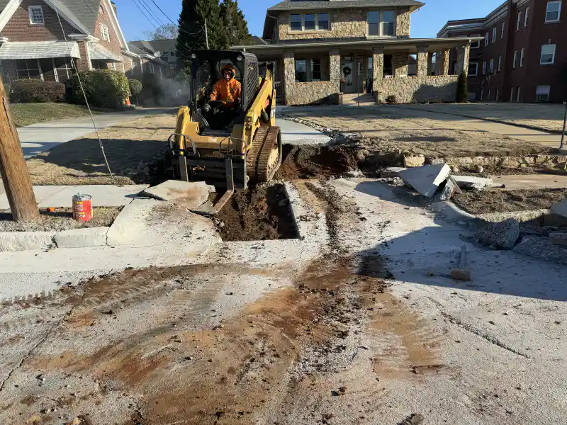 An operator working a skid-steer loader on a residential street during concrete works.