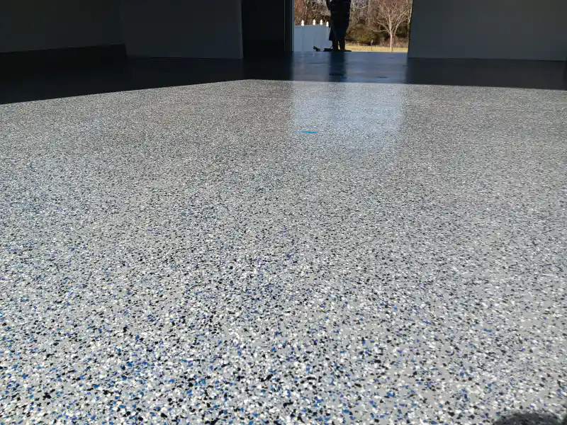 A garage floor finished with a glossy blue, black and white flake epoxy coating, reflecting the open doorway.