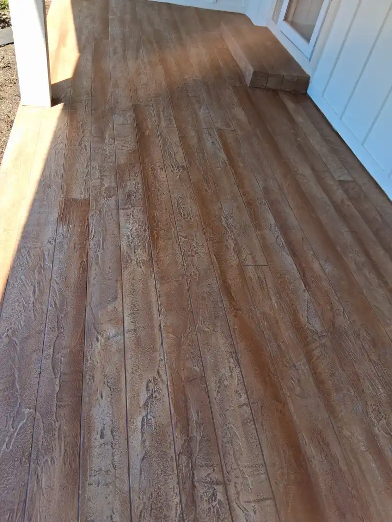 A porch floor finished with a brown wood-plank patterned overlay running the length of the porch to a white door.
