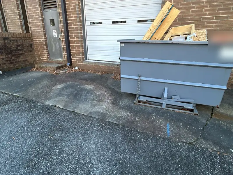A worn asphalt approach and a dumpster below a roll-up loading door on a brick building