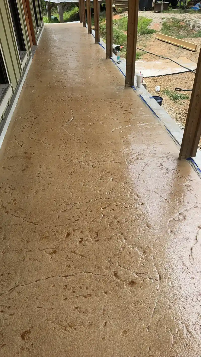 A sand-textured overlay being applied over an existing concrete porch slab, with masking tape and protective sheeting in place.