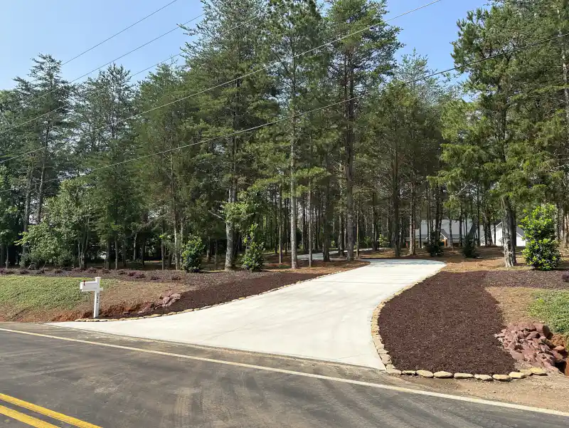 A long finished concrete driveway running downhill to a public road, bordered by mown grass and a mailbox.