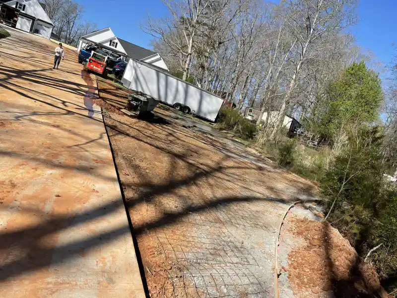 A driveway subgrade with steel reinforcing mesh laid out, beside an existing concrete slab.