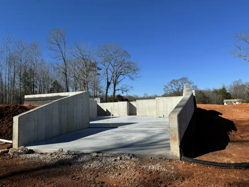 Completed concrete foundation walls enclosing a smooth poured floor slab, with sloped wing walls at either side.
