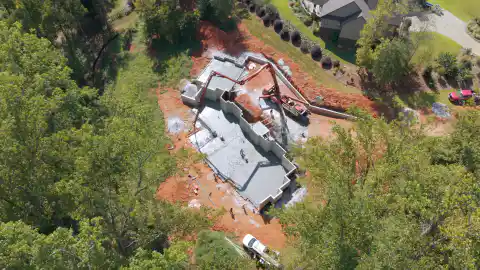 An aerial drone view of a large house foundation with a pump truck's boom extended