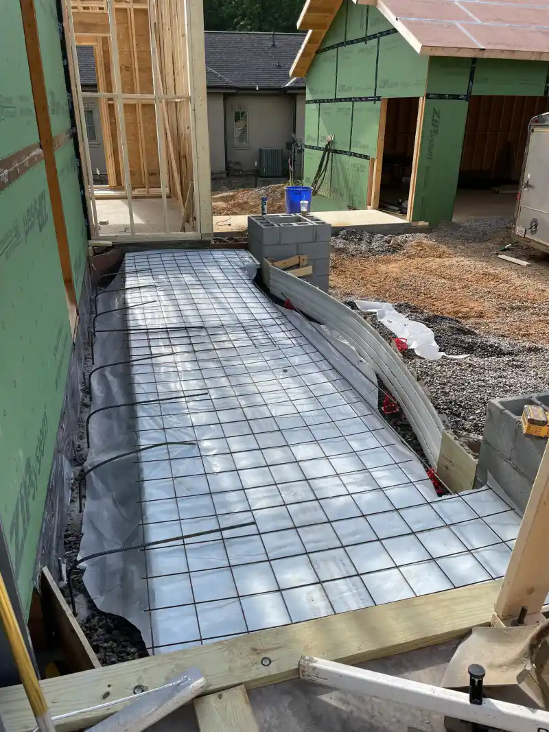 A slab prepared for pouring, showing a plastic vapour barrier beneath a tied steel reinforcing grid and a thickened edge trench.