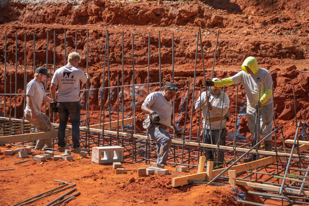 Ace Concrete Construction crew setting rebar and timber forms in an excavated red-clay cut