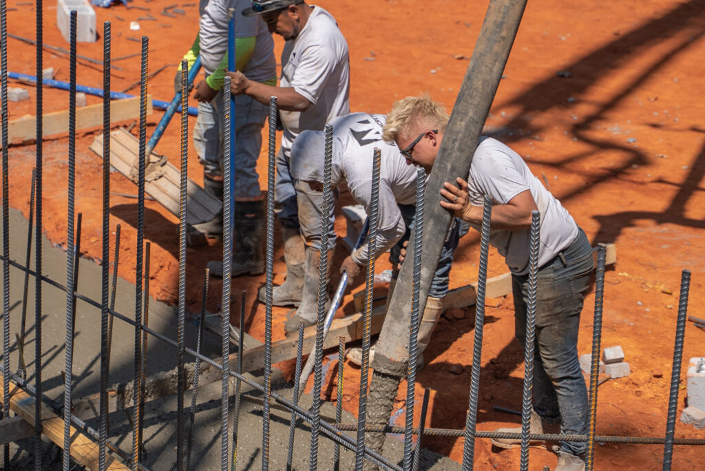 Ace Concrete Construction crew placing concrete from a pump hose into a rebar-reinforced footing